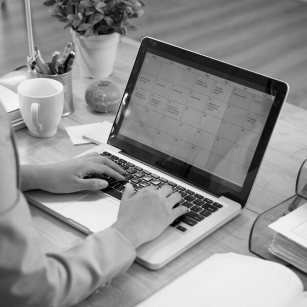 unrecognizable-businesswoman-sitting-desk-with-laptop-looking-calendar